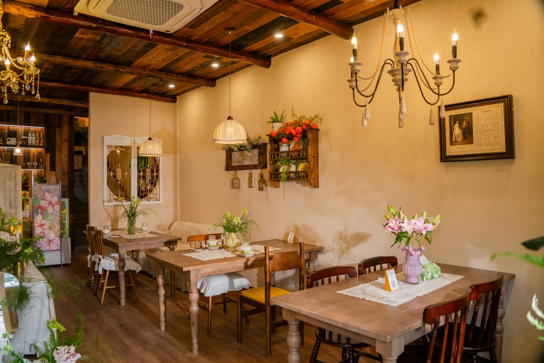 A warm salon with chandeliers, fresh flowers, and wooden tables