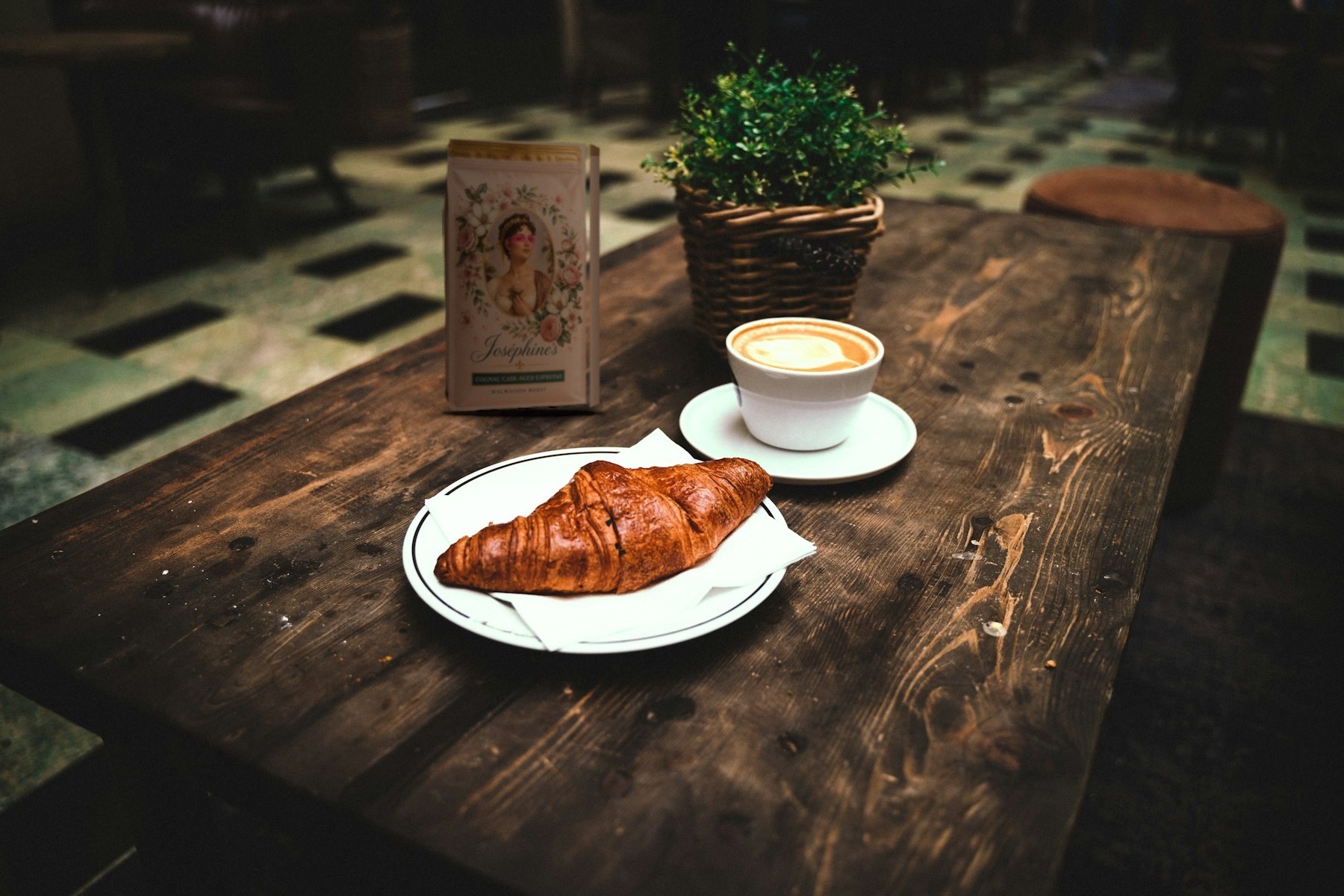 A bag of Joséphine’s Malmaison Roast on a café table beside a croissant and cappuccino