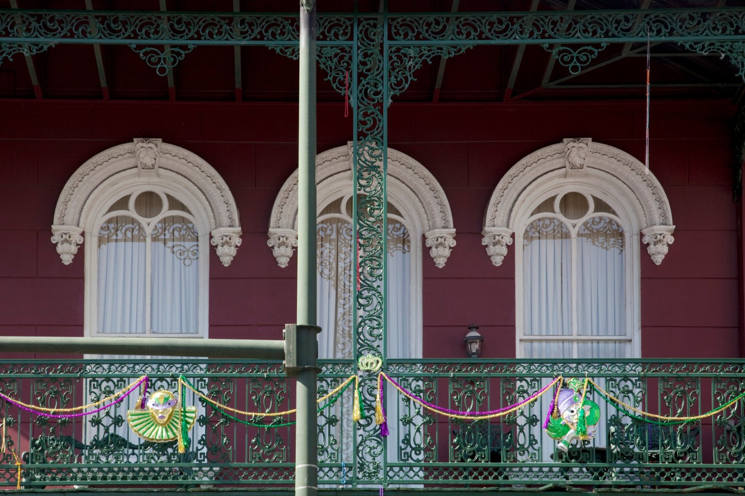 Red façade with arched white windows and ornate green cast-iron balconies on Dauphin Street